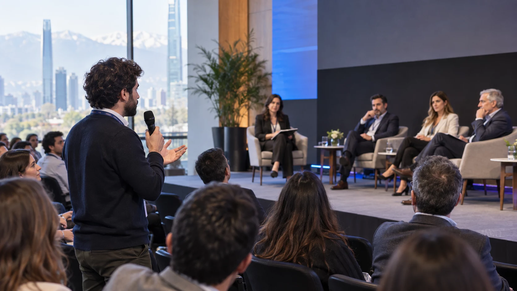 Asistente realizando una pregunta con micrófono inalámbrico durante un panel corporativo